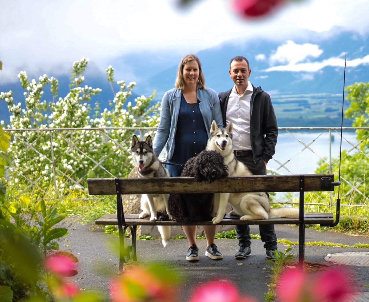 Züchterpaar mit zwei Siberian Huskys und einem Barbet auf einer Bank am See