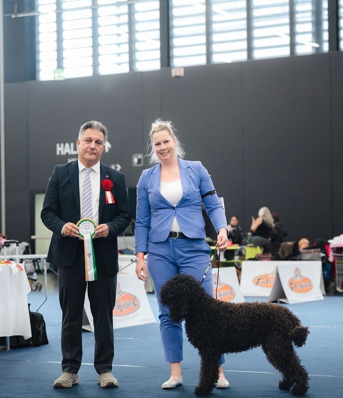 Barbet mit Hundeführerin und Richter nach der Bewertung im Ausstellungsring